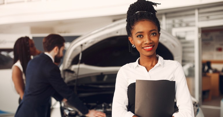 Car saleswoman standing in front of a car at dealership