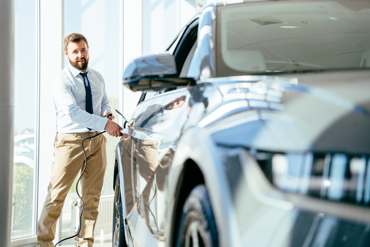 Professional car salesman plugging in an electric car at a dealership