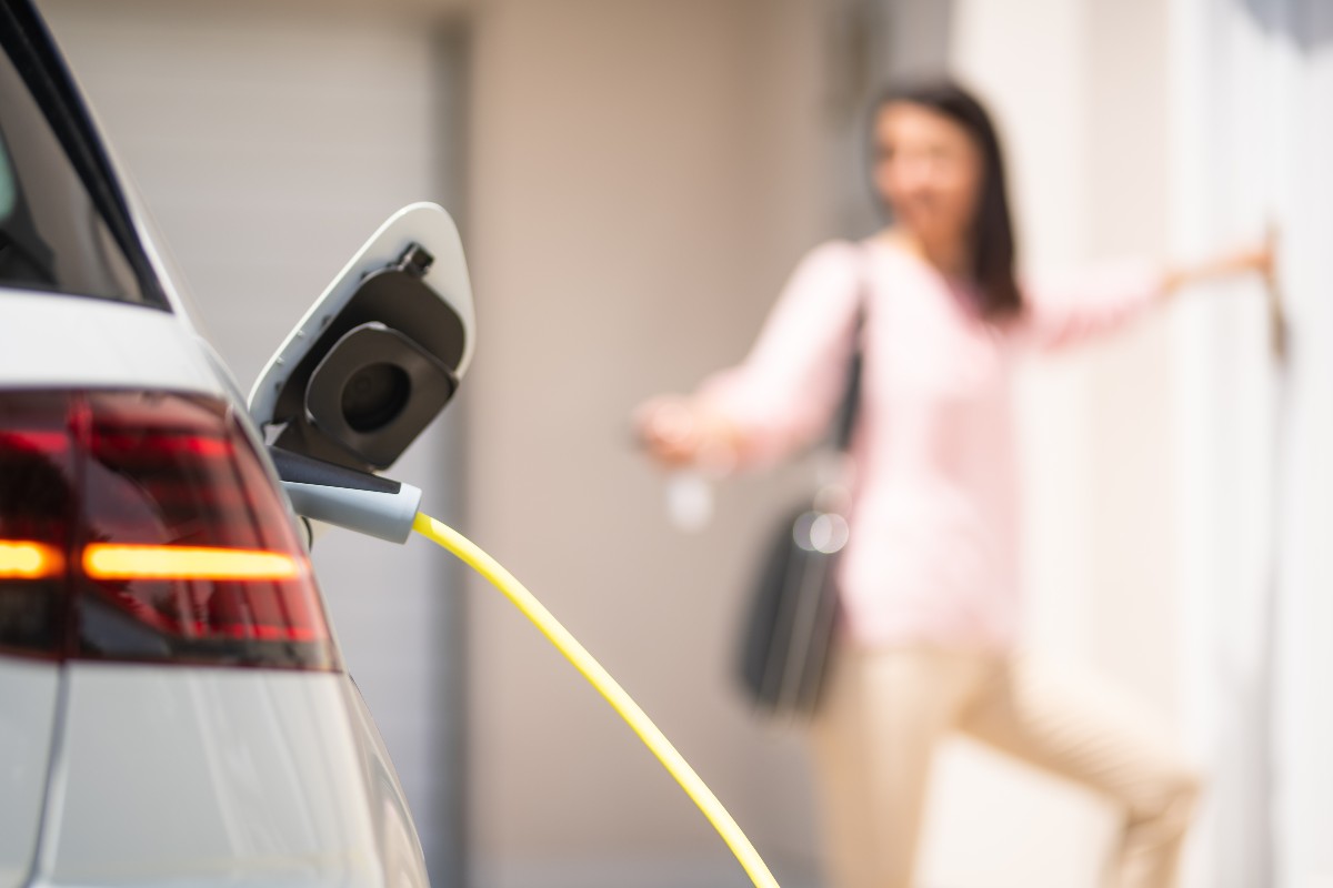 Electric Vehicle charging with woman in the background holding keys out to unlock