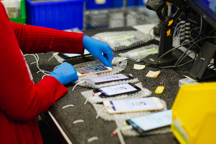 Women in red sweater wearing plastic gloves is tagging various mobile phones in a repair depot
