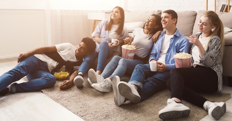 group of friends sitting on floor eating popcorn watching TV
