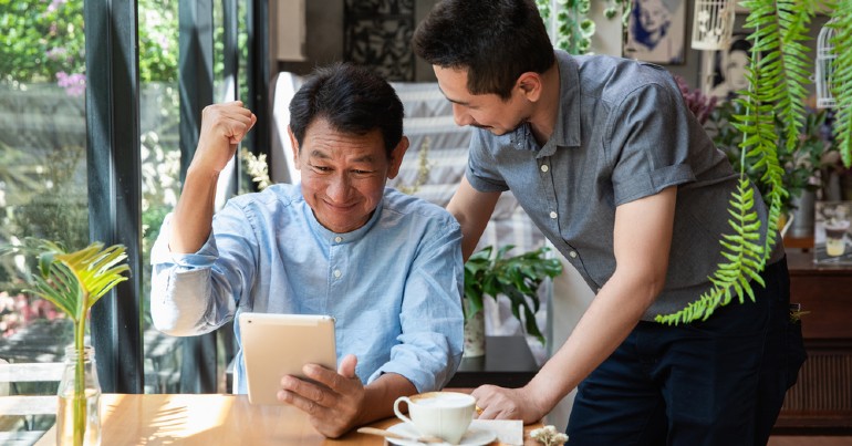 man sitting down with tablet receiving support from another man beside him
