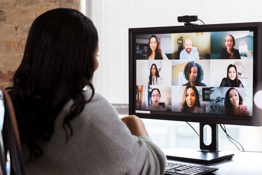 Woman seating at her desk looking at a computer screen and participating on a zoom call