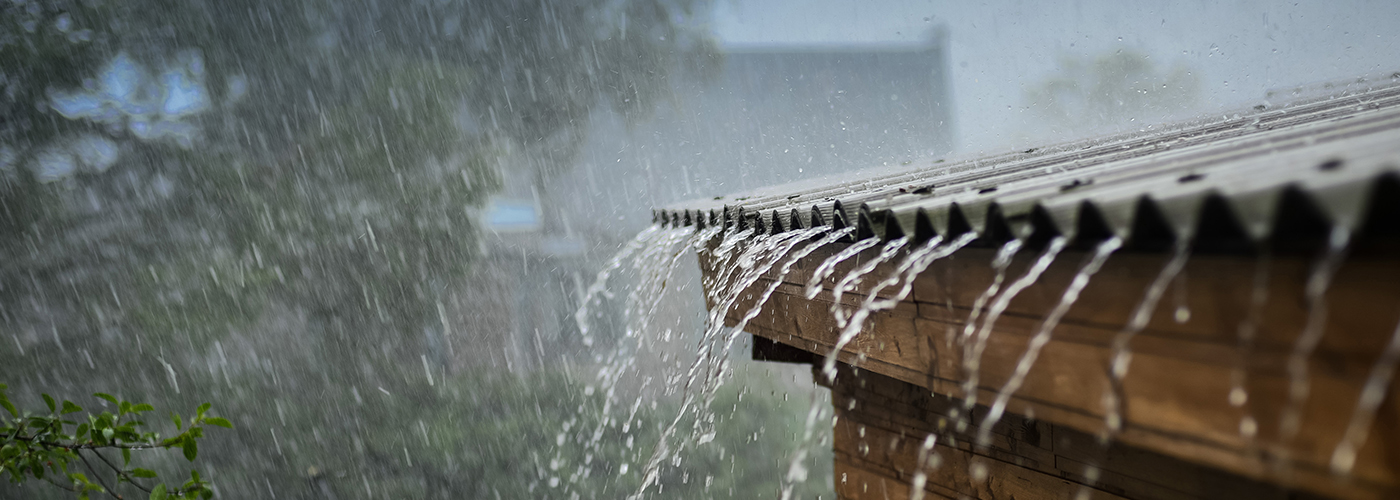 FLOOD-rain roof-Getty-547033564-LR Hard rain dripping of a metal roof with trees in the background