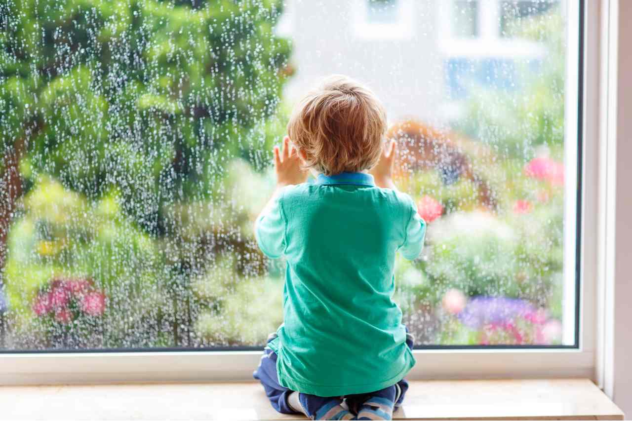 boy in green shirt watching sunshine come through rain in window