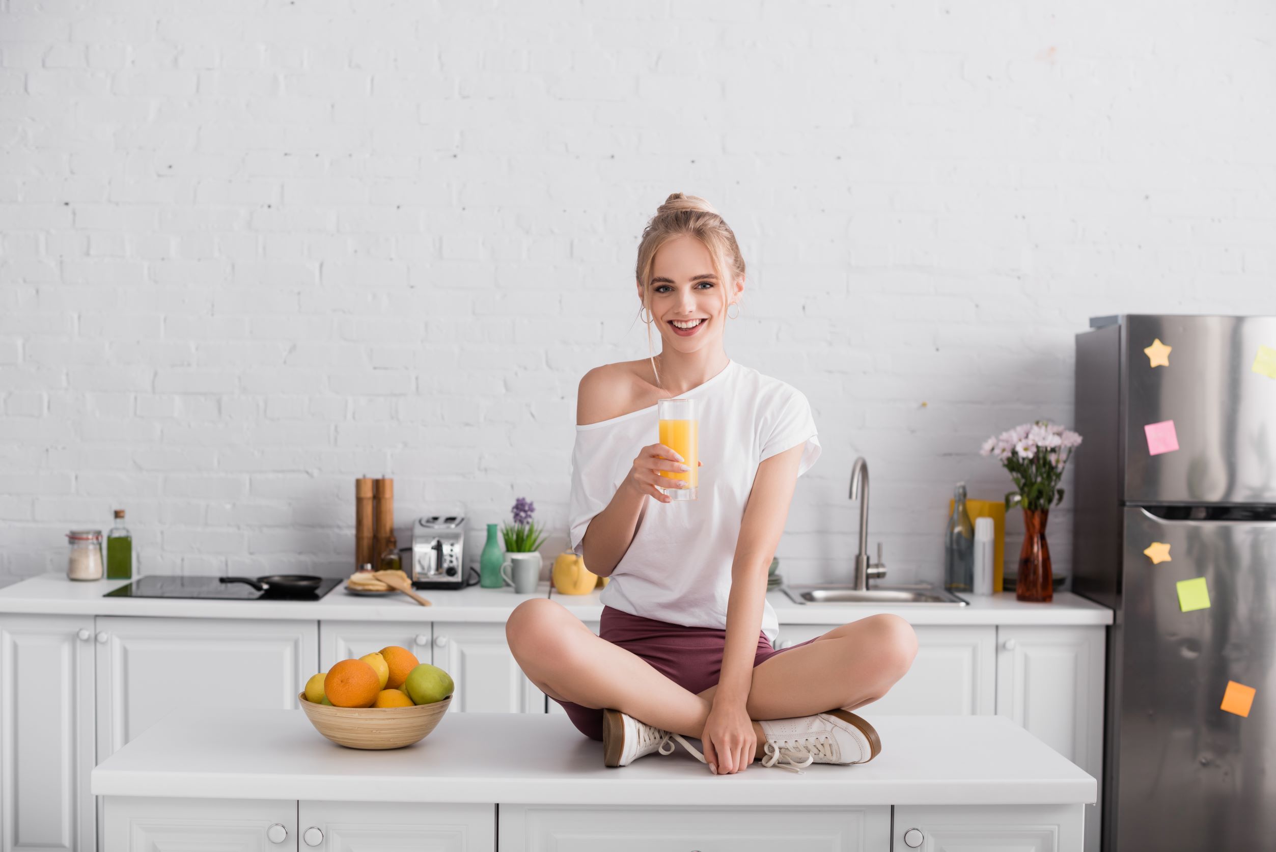 Woman sitting on kitchen counter with her legs crossed and drinking orange juice