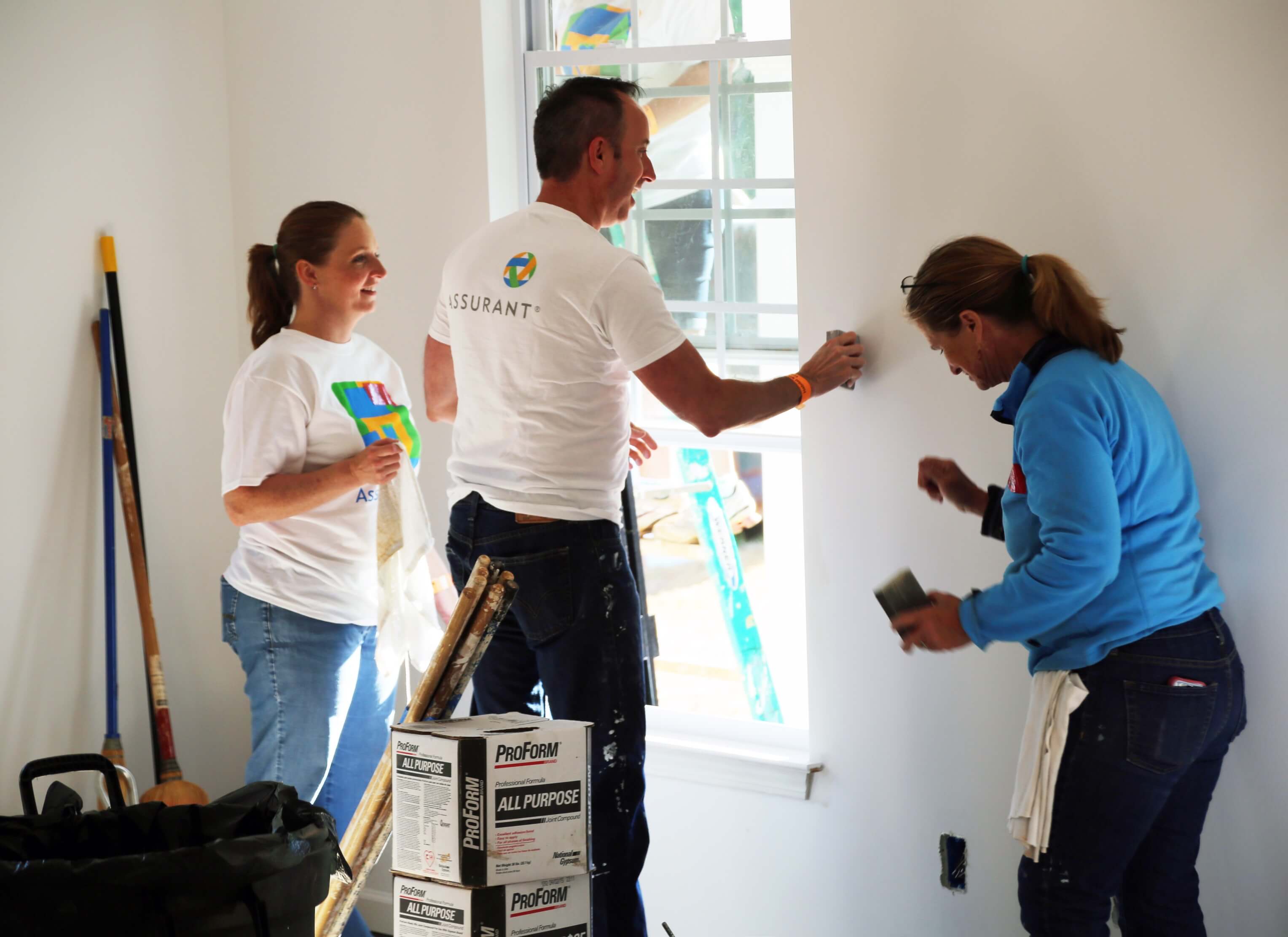 three assurant employees working at a Habitat for Humanity build sanding walls